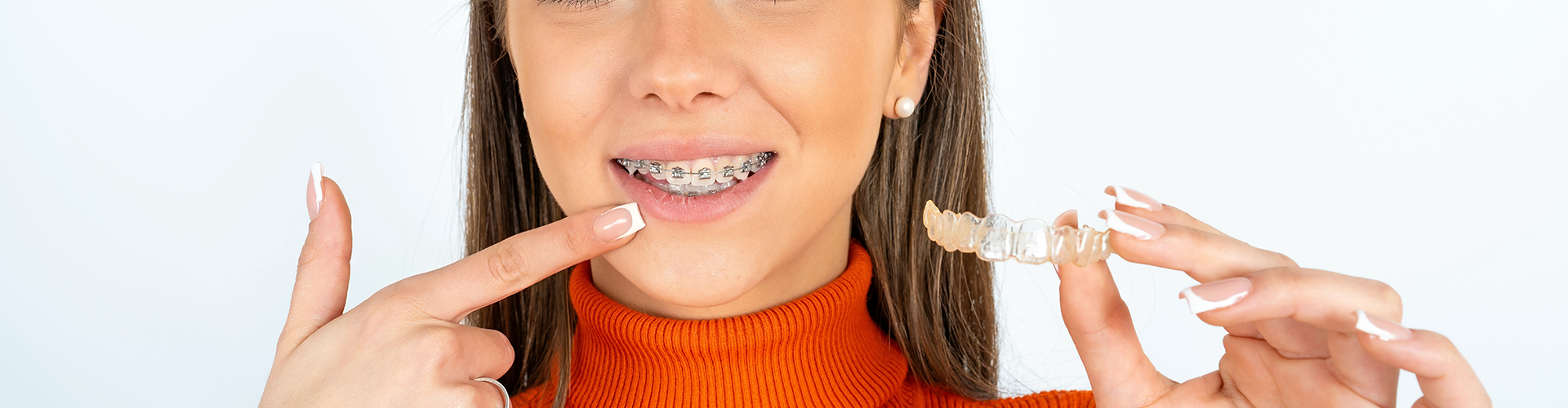 woman pointing to braces on teeth and holding clear aligner